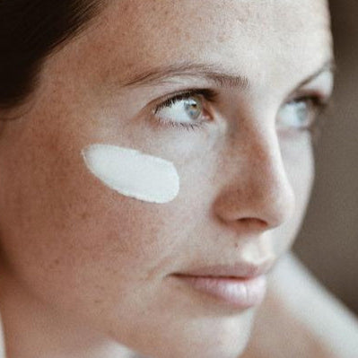Close-up of a woman's face with a skincare product applied to her cheek.