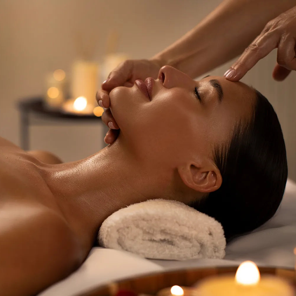 Woman receiving a facial massage in a spa setting with candles and towels.