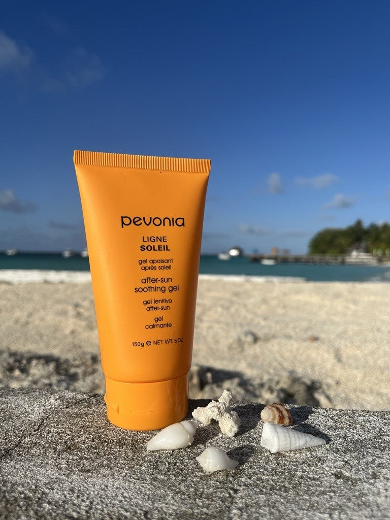 Orange tube of Pevonia sunscreen gel on a beach with ocean and sky in the background
