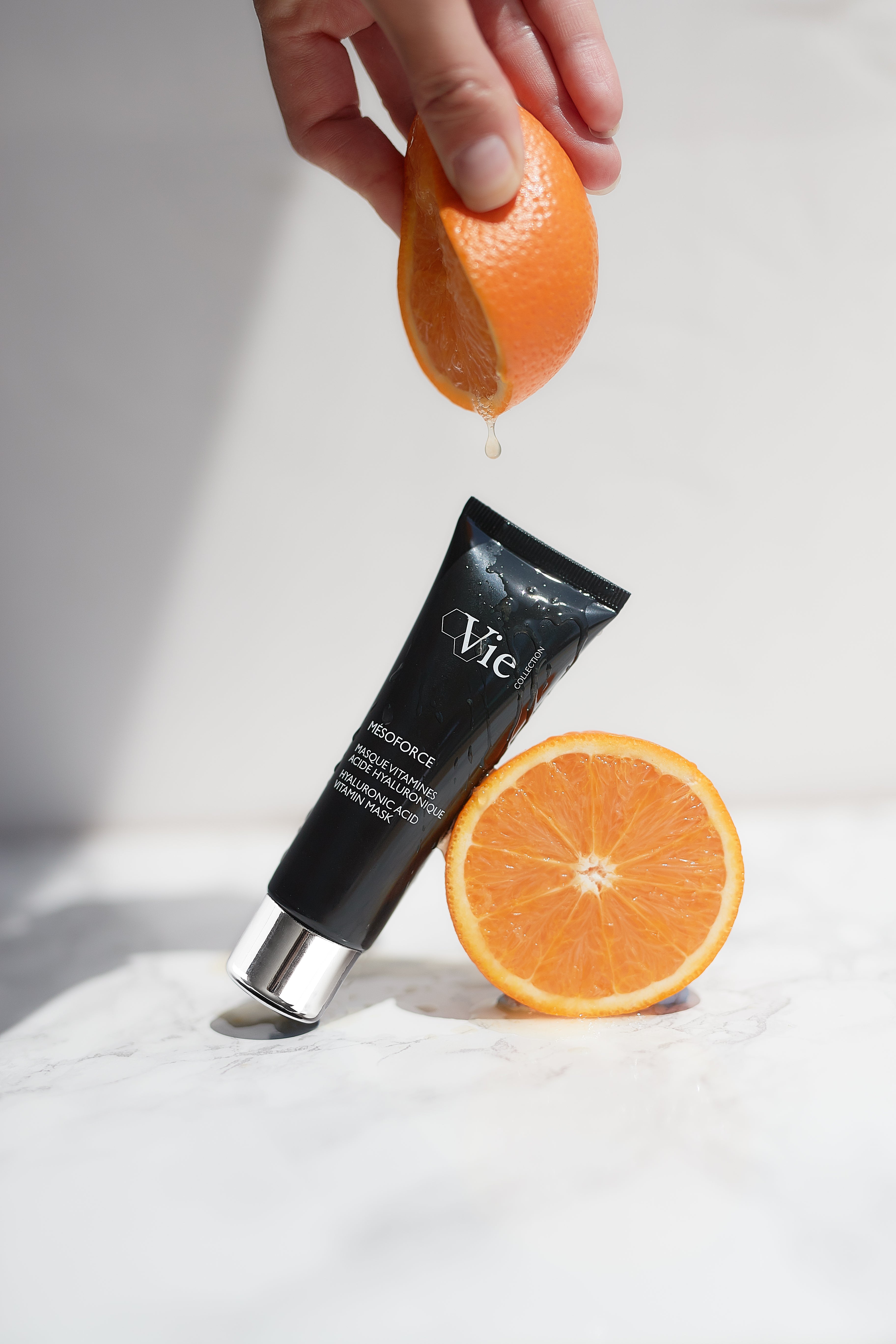 Tube of Vie skincare product with an orange being squeezed over it on a white surface