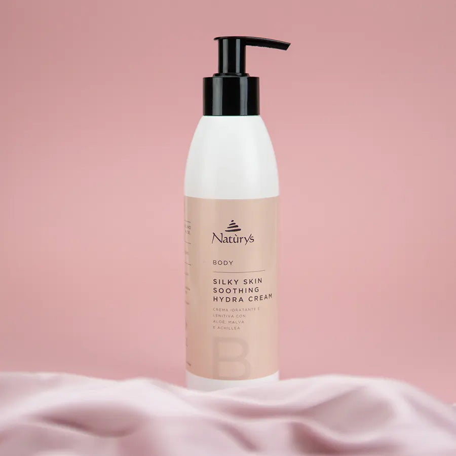 A pump bottle of Naturys Silky Skin Soothing Hydra Cream against a pink background, designed for body moisturization.