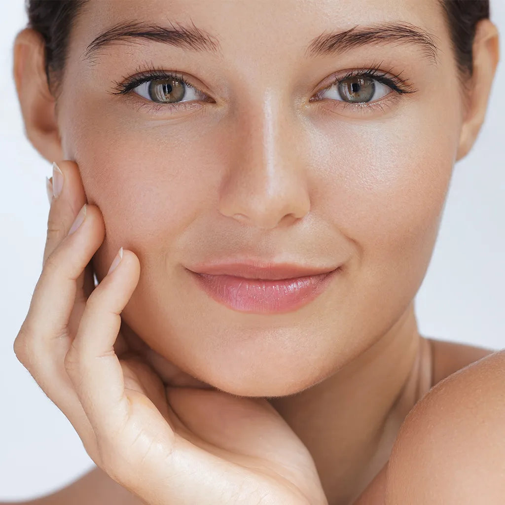 Close-up of a woman's face with a soft smile, touching her cheek against a neutral background