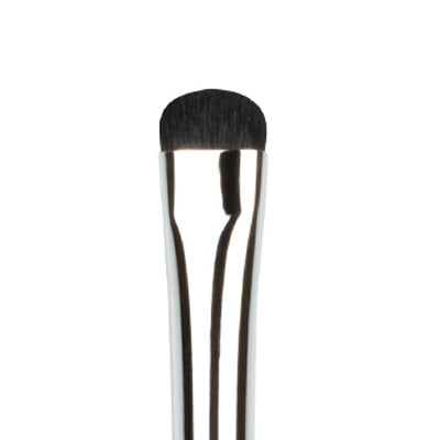 A close-up image of a flat makeup brush with Taklon bristles, showing the brush's head with dense, black bristles arranged in a flat pattern, and a silver metal handle.