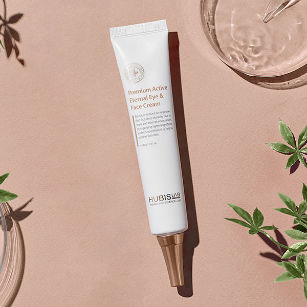 Tube of Hubis Lab Premium Active Eternal Eye & Face Cream on a beige background with plant elements.