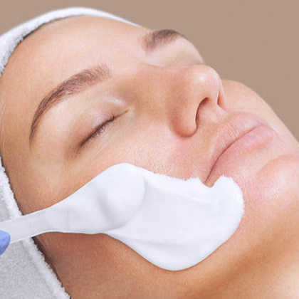 Person receiving a facial treatment with a white cream on a beige background