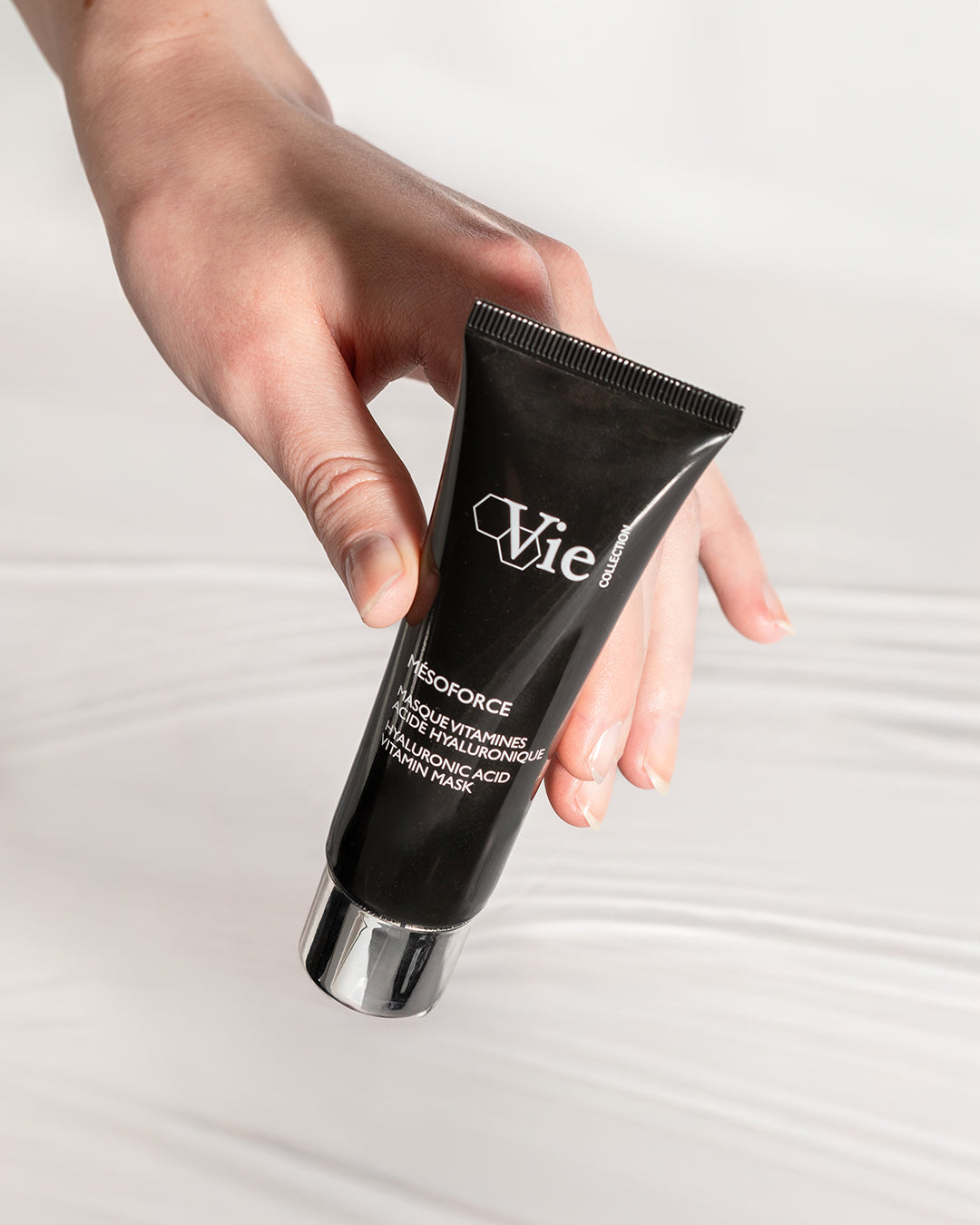 Hand holding a black tube of Vie skincare product on a light gray background