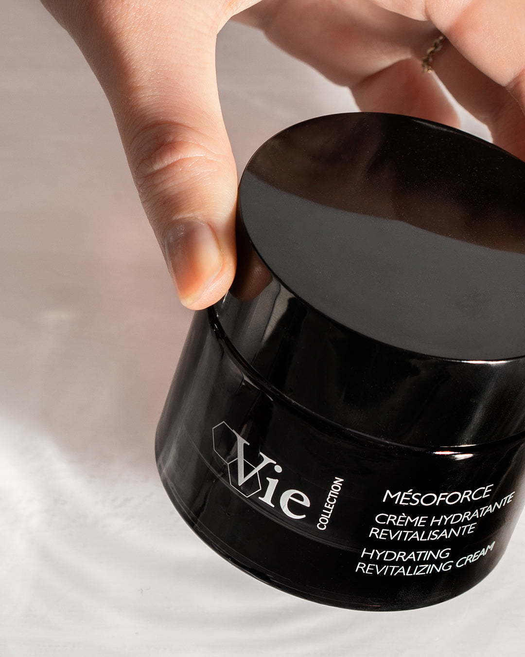 Black jar of Vie skincare cream with a hand lifting the lid.
