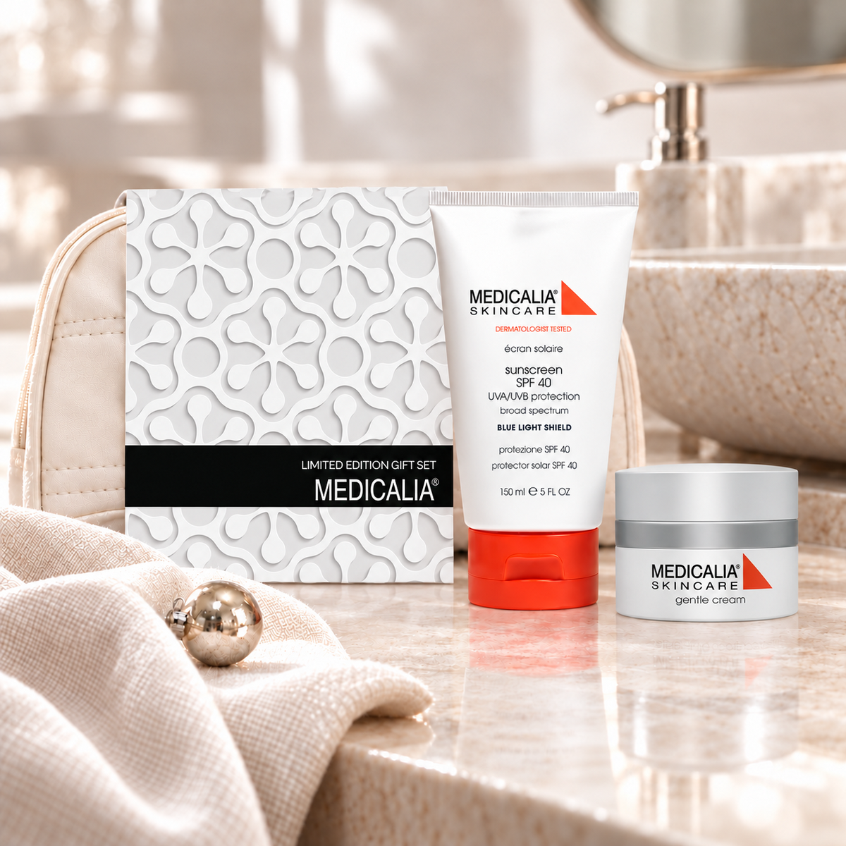 A Medicalia Skincare limited edition gift set arranged on a bathroom counter, including a boxed set, a sunscreen tube with an orange cap, and a cream jar, with a beige textured bag and soft neutral decor in the background.