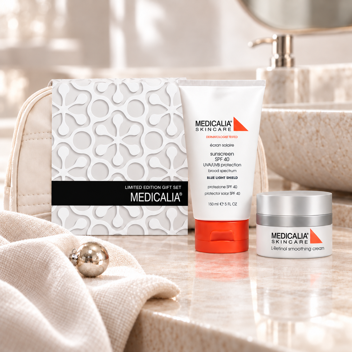 A Medicalia Skincare sun protection set arranged on a bathroom counter, including a boxed set, a sunscreen tube with an orange cap, and a cream jar, with a beige textured bag and soft neutral props in the background.