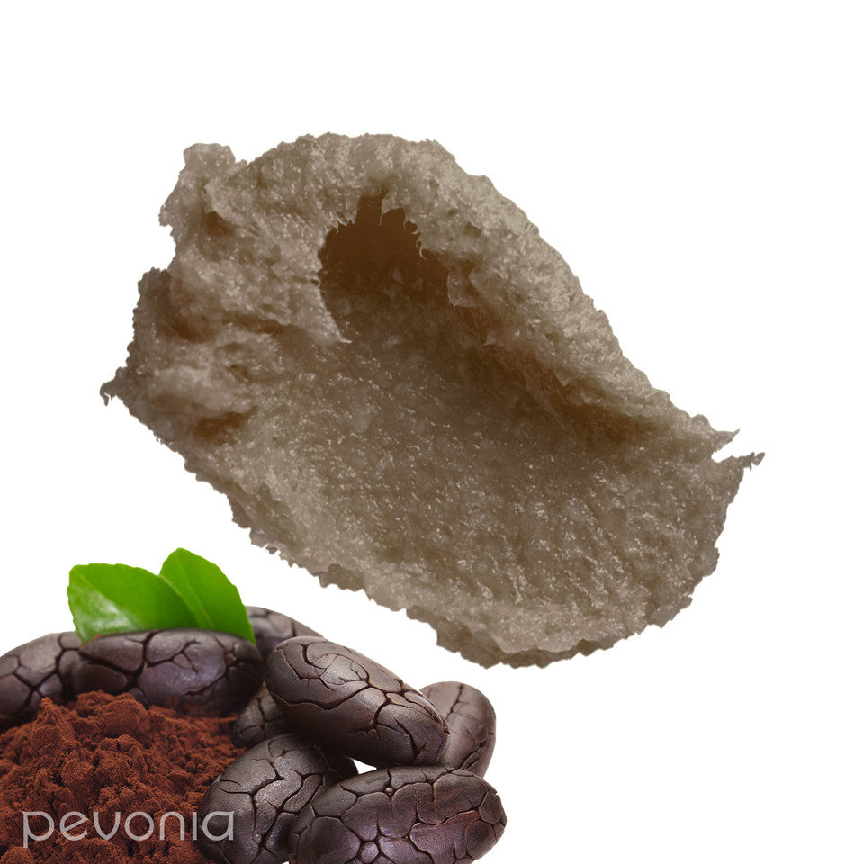 Pevonia Chocolate Indulgence Foaming Salt Scrub indicating Texture and ingredients, Close-up of a smear of brown scrub with a green leaf on a white background, featuring the brand 'Pevonia'.