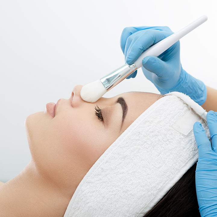 Person receiving a cosmetic procedure with a brush and gloved hands on a white background