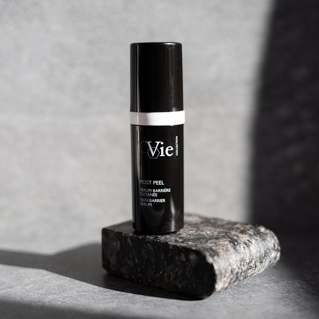 Skincare serum bottle labeled 'Vie' on a stone surface with a gray background