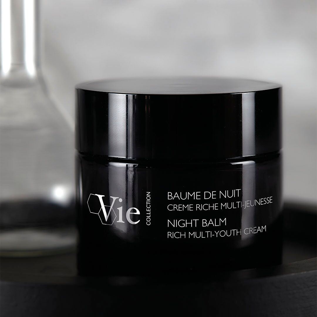 Black jar of Vie Night Balm on a reflective surface with a blurred background