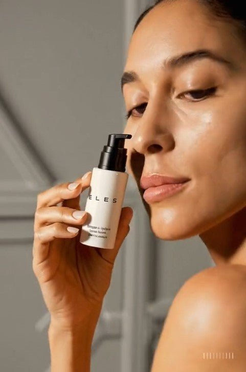 Woman holding a skincare product labeled 'ELES' against a neutral background