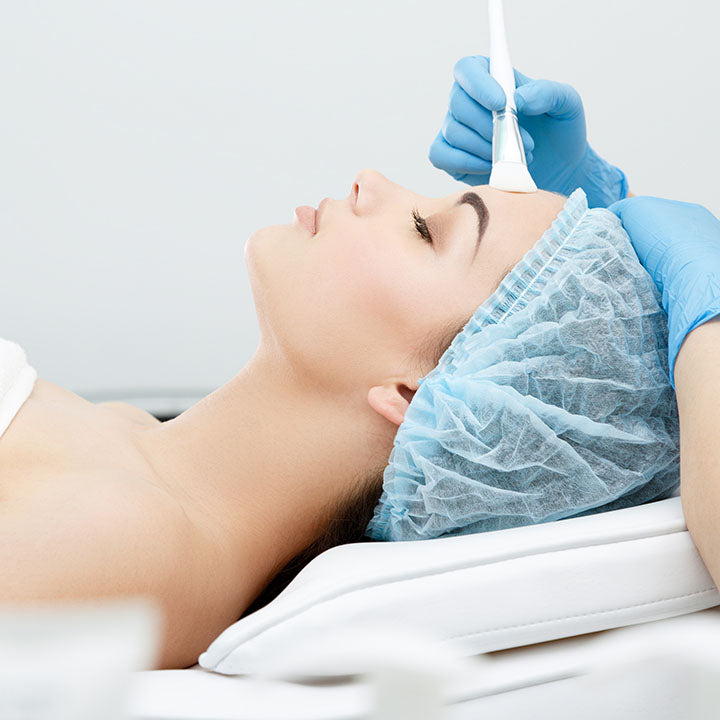 Woman receiving a cosmetic procedure with a gloved hand holding a tool.