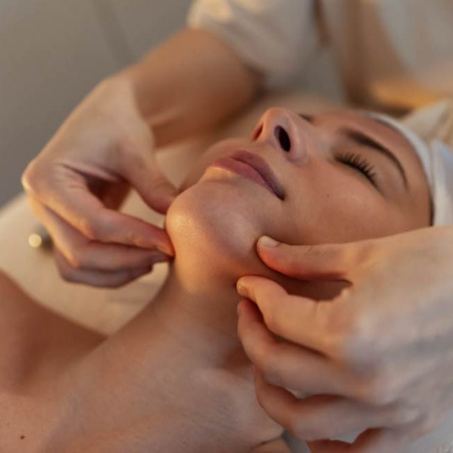 Person receiving a facial massage with hands applying pressure to the face.