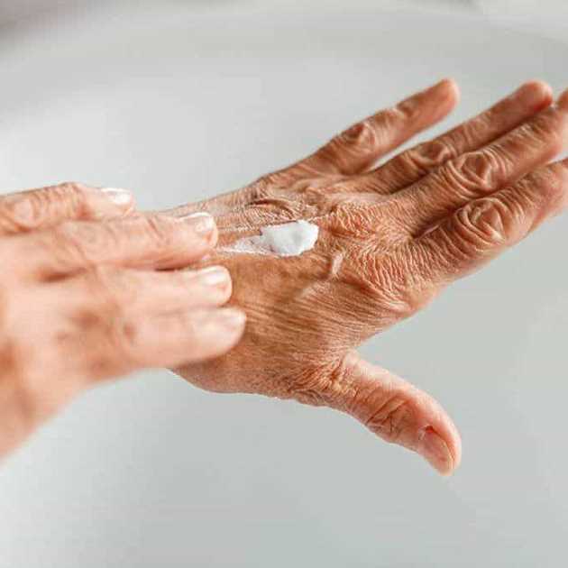 Close-up of hands applying cream to another hand on a light background