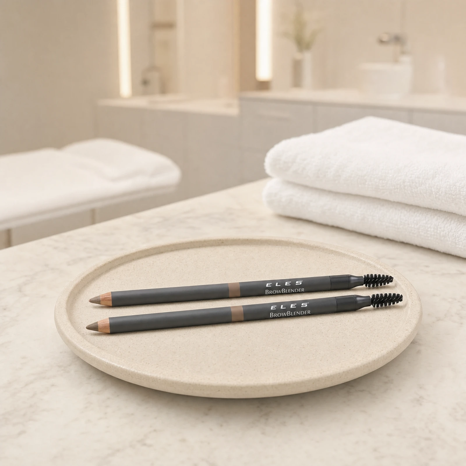 ELES Brow Blender Pencils in two shades resting flat on a stone tray on a marble clinic bench inside a premium skin clinic treatment room, showing the full dual-ended pencil and spoolie brush design