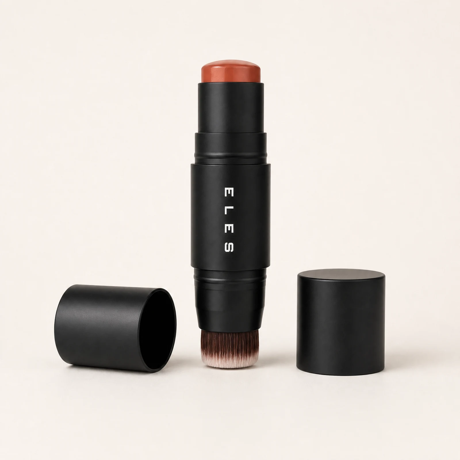 ELES cheek and lip cream with Brush with a black cylindrical body, a warm terracotta-colored cosmetic stick top, and a dual-ended brush bristle base. The main stick stands upright in the center, with its black cap lying on its side to the left and another black cap standing to the right, all on a clean off-white background.