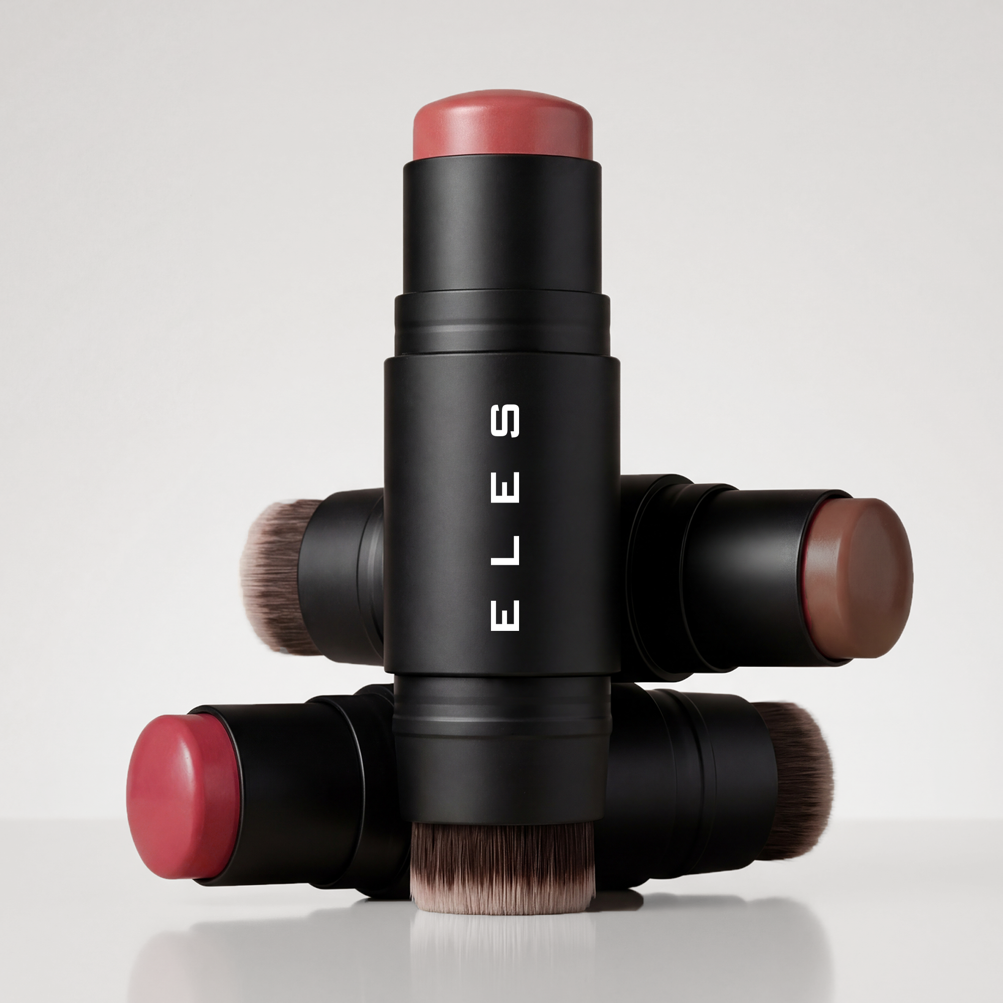 ELES Cheek & Lip Cream Stick collection featuring multiple shades with integrated blending brushes, shown in premium black packaging on a clean neutral background