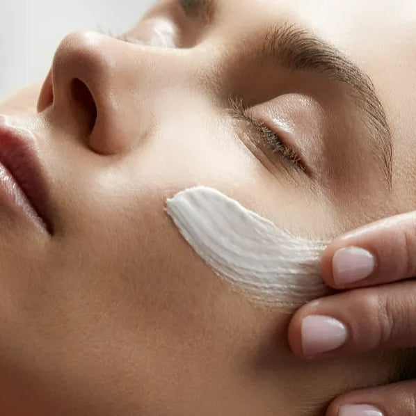 Close-up of a person applying white cream to their face with a finger.