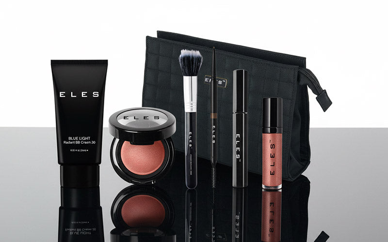 Makeup products including a brush, compact, and lip gloss with 'ELES' branding on a reflective surface.