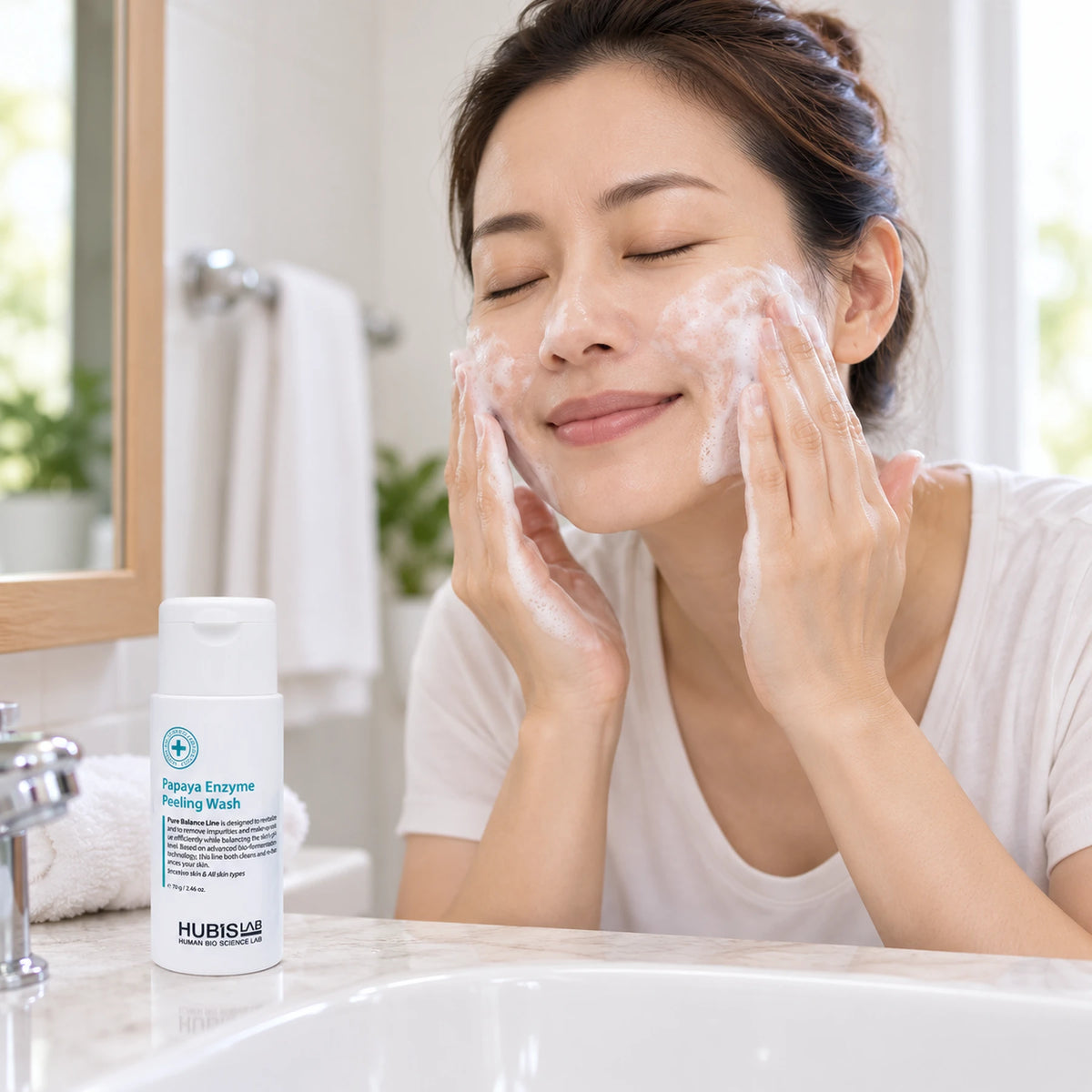 Woman using HUBISLAB Papaya Enzyme Peeling Wash during facial cleansing at home, with the 70 g bottle beside the basin.
