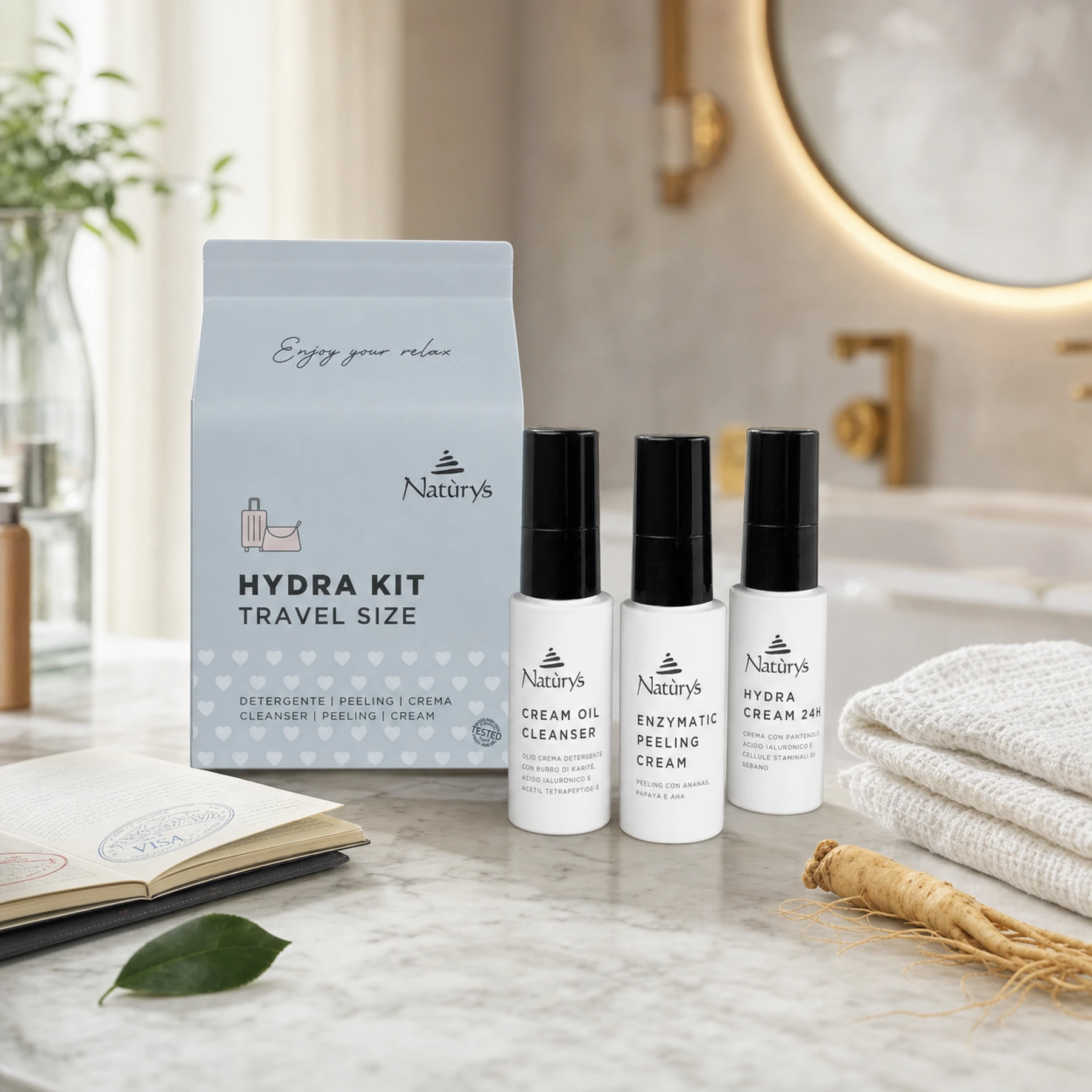 Naturys Hydra Kit Travel Set with Cream Oil Cleanser, Enzymatic Peeling Cream and Hydra Cream 24H three 30ml bottles and soft blue-grey travel pouch on a white marble vanity with open passport, camellia leaf, ginseng root and white waffle linen cloth in a luxury hotel spa bathroom setting
