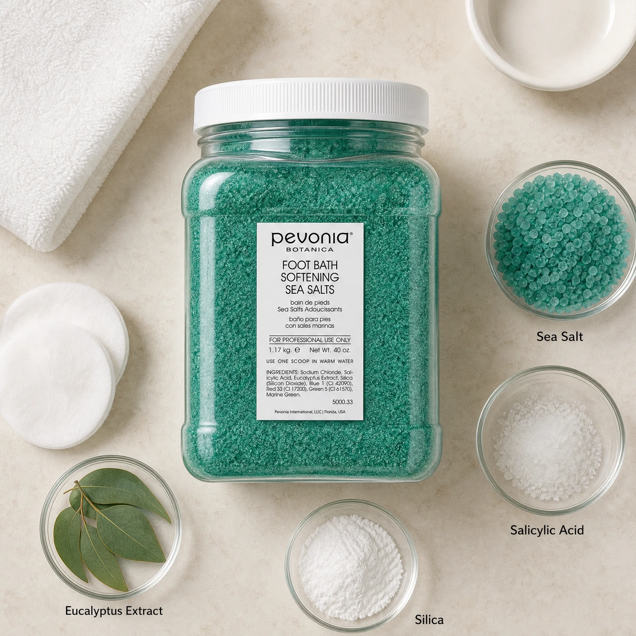 Pevonia Botanica Foot Bath Softening Sea Salts 1.17kg ingredients flatlay with teal-green sea salt crystals, salicylic acid, eucalyptus leaves, and silica in clean glass petri dishes for professional B2B education.