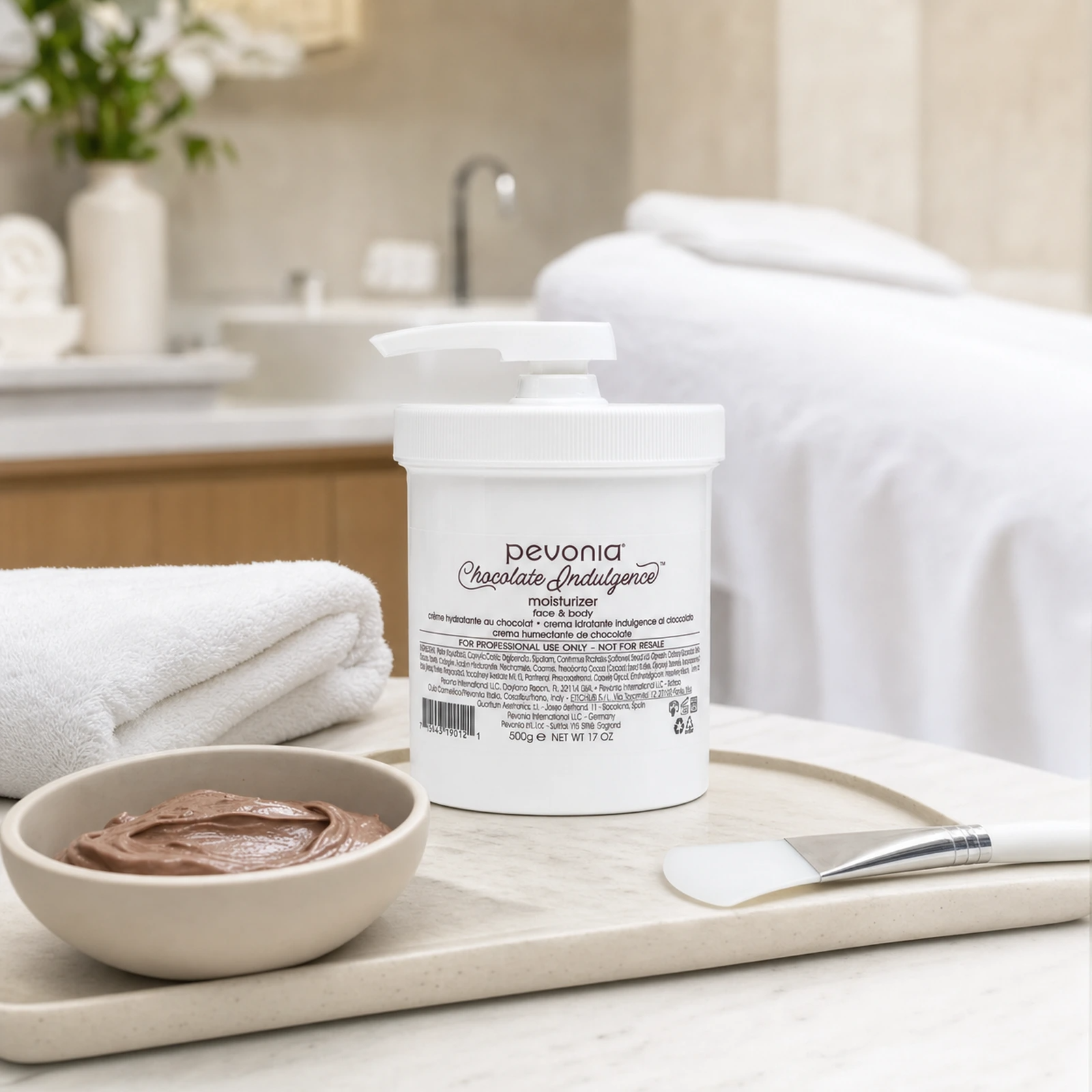 Pevonia Chocolate Indulgence Moisturizer 500g jar displayed in an upmarket body treatment room with a treatment trolley, folded towels and body wrap preparation accessories.