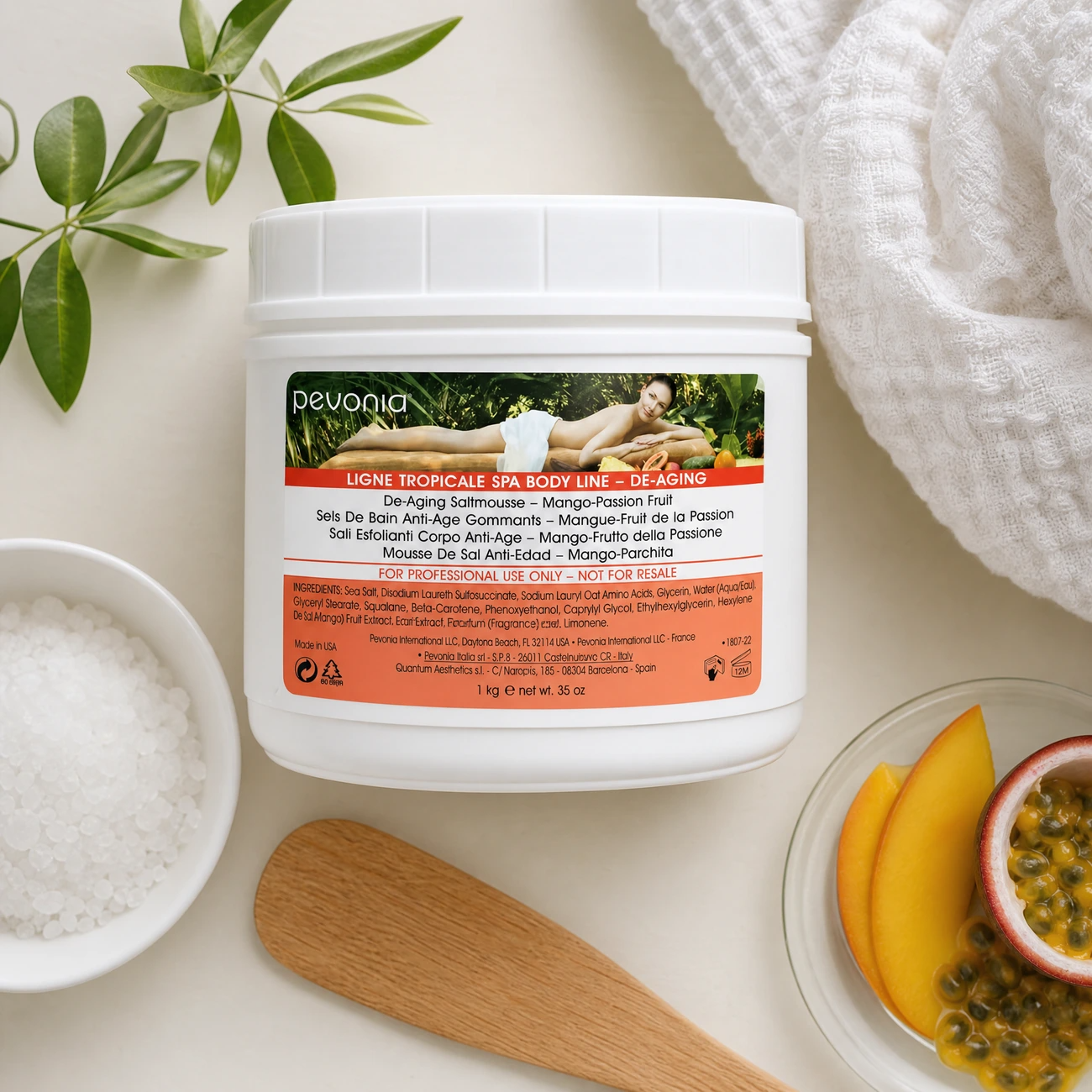 Pevonia De-Ageing Saltmousse Mango Passionfruit 1kg treatment-support flatlay with sea salt, mango, passionfruit, wooden spatula and professional body treatment tools.
