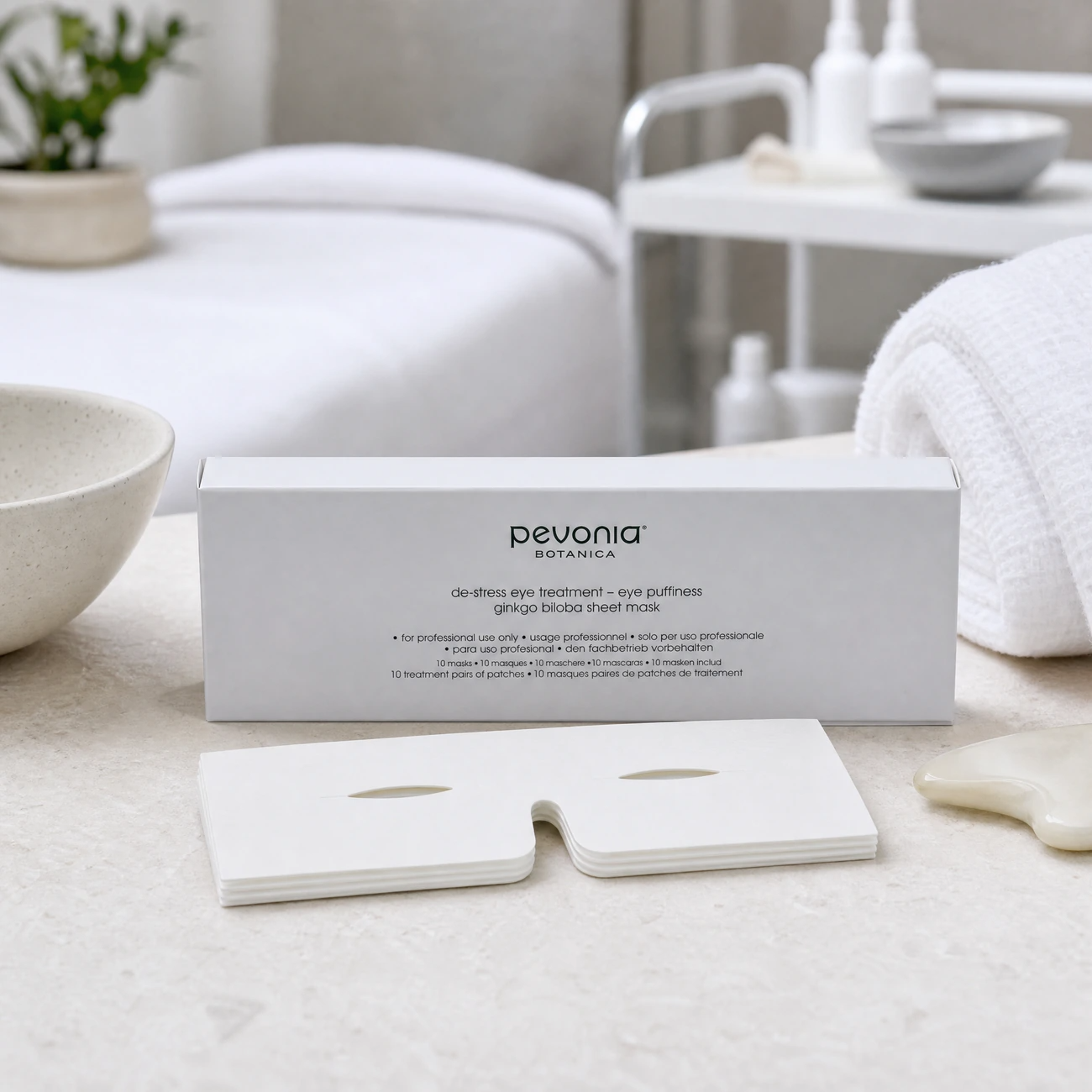 Pevonia Botanica De-Stress Eye Puffiness Ginkgo 10-pack box and flat white eye sheet masks styled in a serene clinical spa treatment room for Beauty Collective Pro.