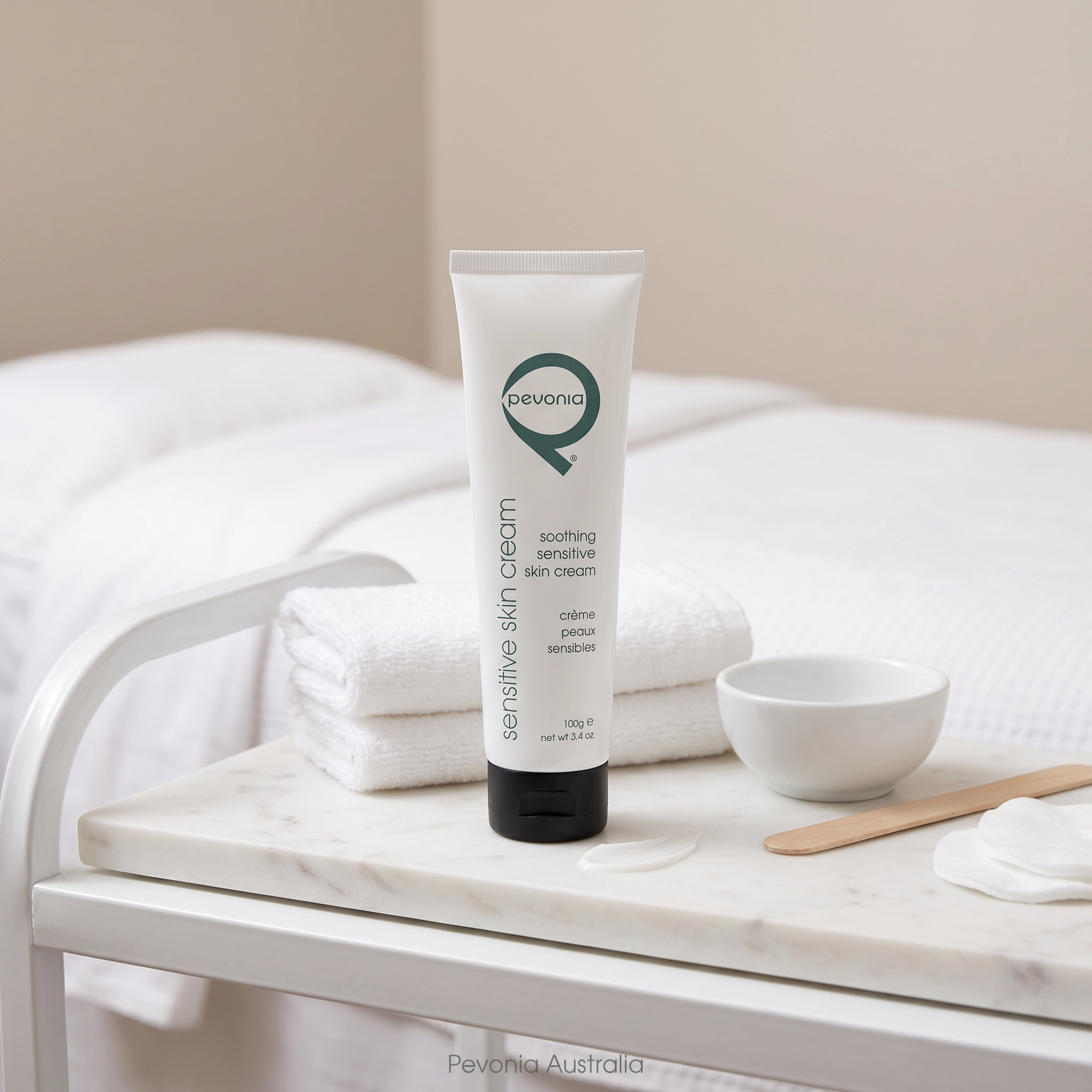 Pevonia Soothing Sensitive Skin Cream 100g professional facial treatment cream displayed on treatment trolley with folded towels bowl spatula and texture sample in clinical spa environment for calming sensitive skin treatments