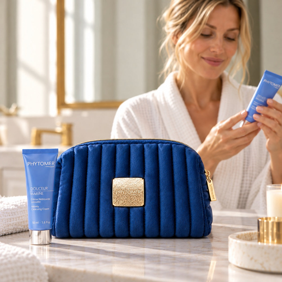 PHYTOMER Douceur Marine Ritual Gift Set in a bathroom setting with blue pouch and woman holding skincare tube.