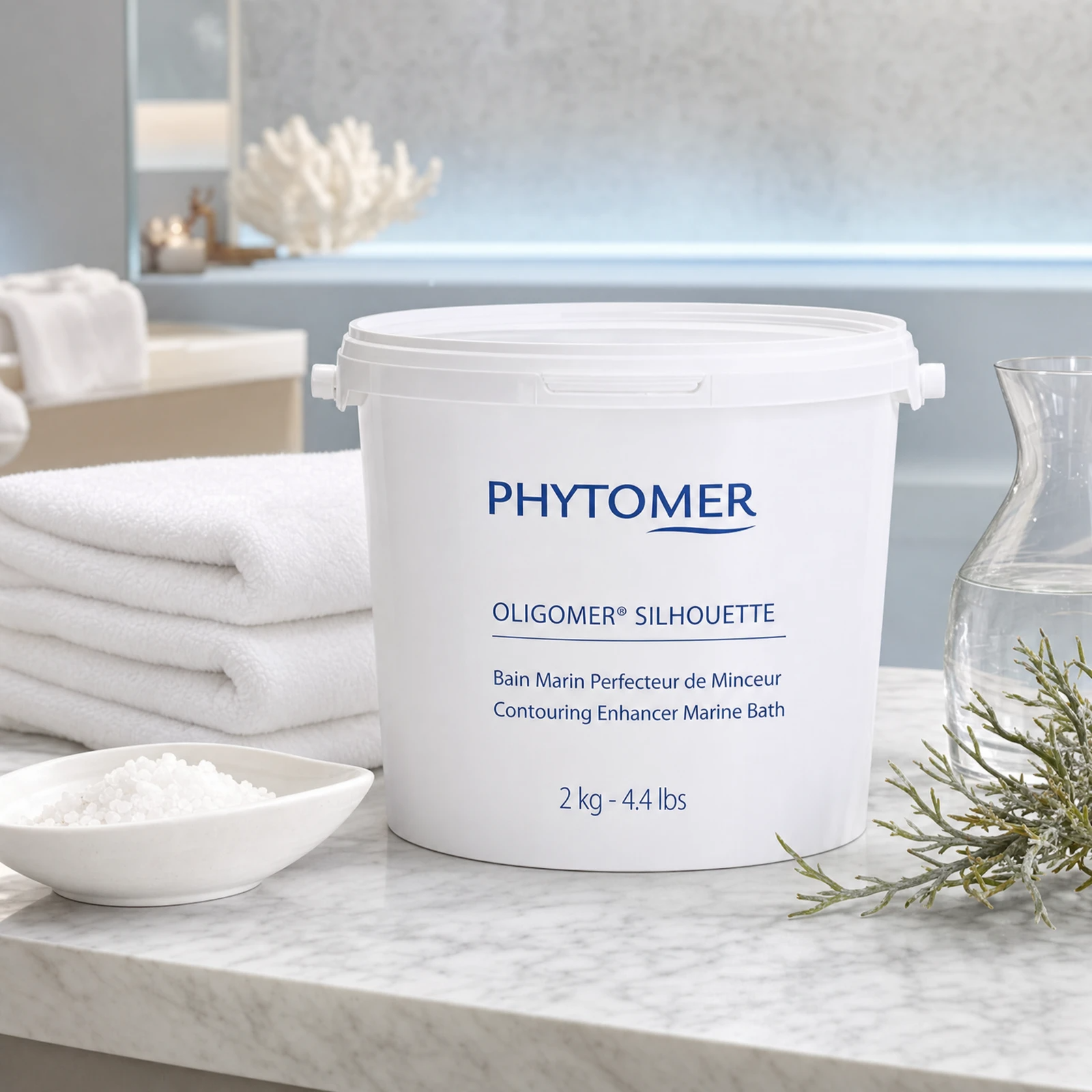 Phytomer Oligomer Silhouette Contouring Enhancer Marine Bath 2kg tub on a marble spa treatment counter with mineral crystals in ceramic dish, glasswort sprig, glass carafe, white coral, white spa towels and blue-lit bathtub in background, professional clinic setting