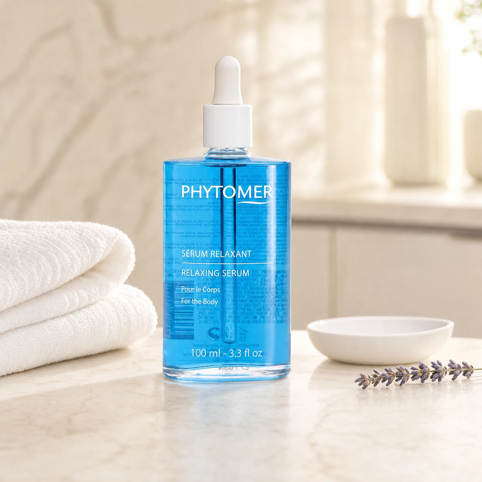 Phytomer Relaxing Serum for the Body 100ml blue glass dropper bottle on a premium spa treatment marble counter with white towels, ceramic dish and dried lavender