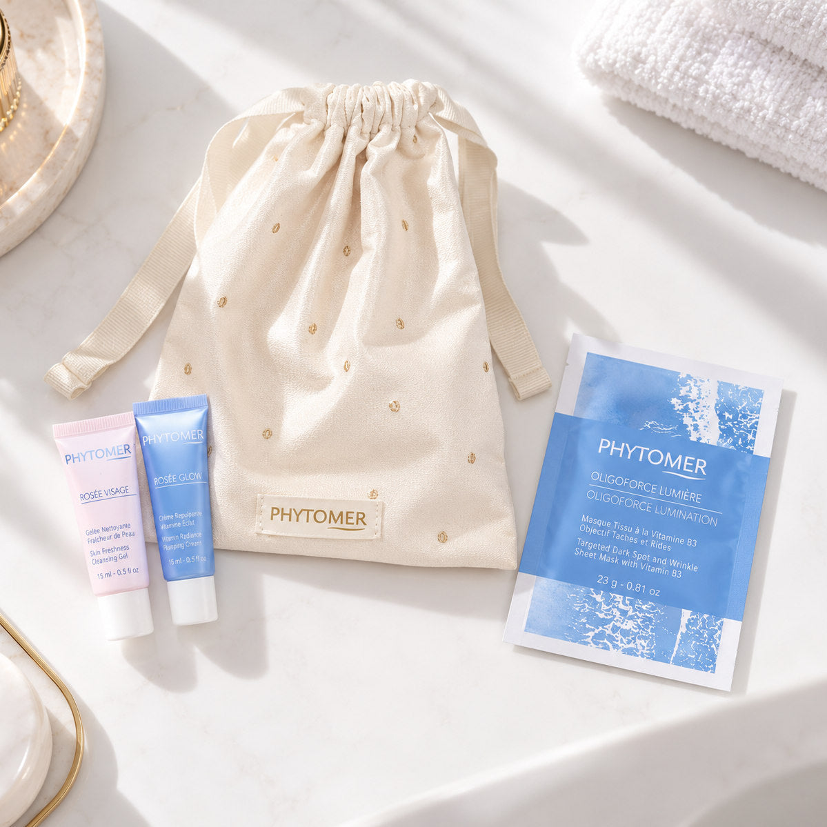 PHYTOMER Ritual Glow Gift Set flat lay featuring ivory drawstring pouch, two 15 ml skincare tubes and Oligoforce Lumière sheet mask.