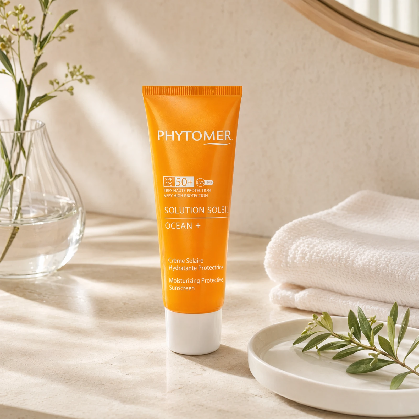 Phytomer Sun Solution Ocean+ SPF50 Moisturizing Protective Sunscreen 50ml on a marble bathroom vanity with botanical, glass vessel, white towels and ceramic dish, premium at-home skincare setting