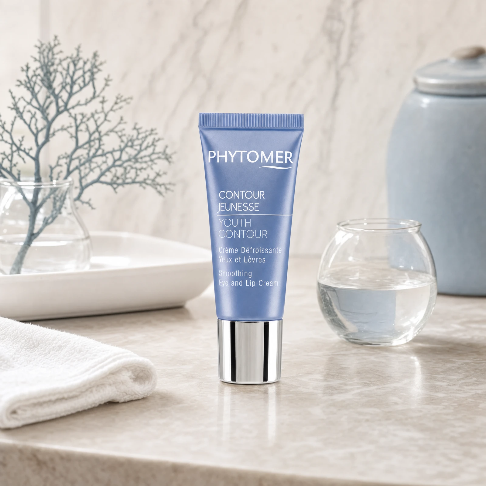 Phytomer Youth Contour Smoothing Eye and Lip Cream on a marble bathroom vanity with ceramic tray, glass vessel, sea coral botanical and white towel, premium at-home skincare setting