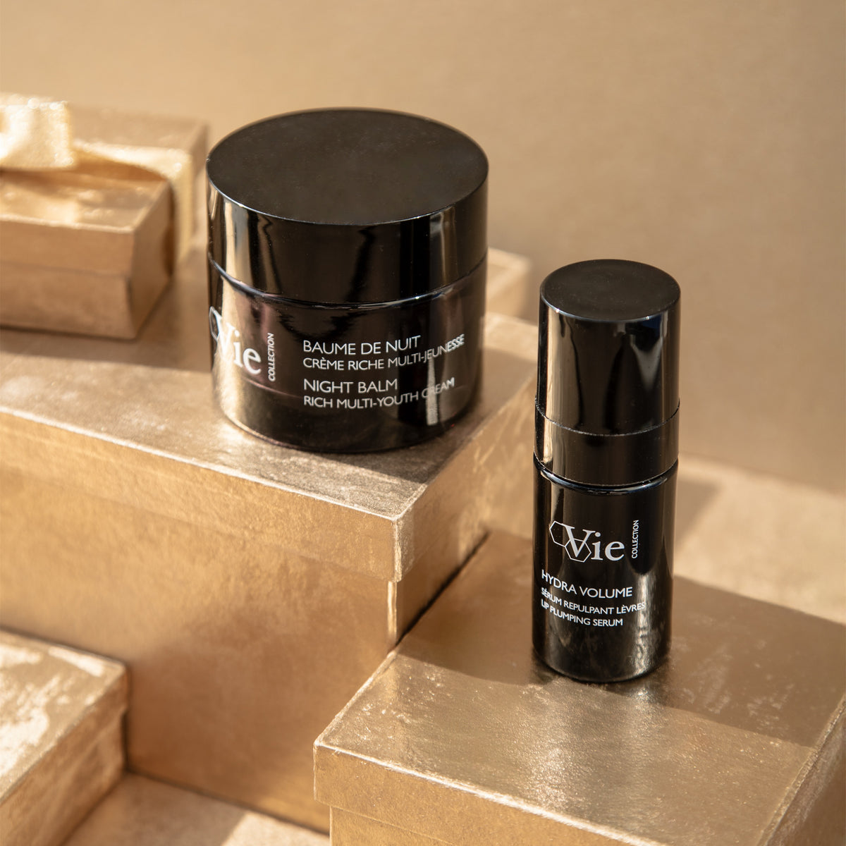 Vie Collection Night Balm Rich Multi-Youth Cream and Hydra Volume Lip Plumping Serum displayed on gold gift boxes.