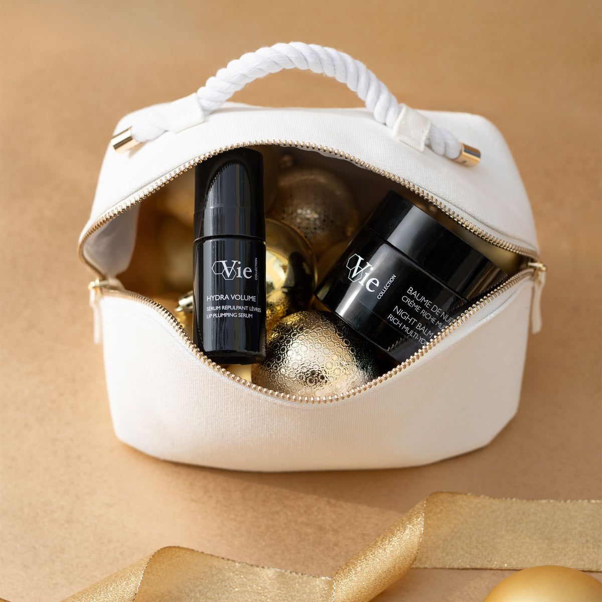Vie Collection Night Balm and Hydra Volume Lip Plumping Serum in an open white pouch with gold Christmas baubles.
