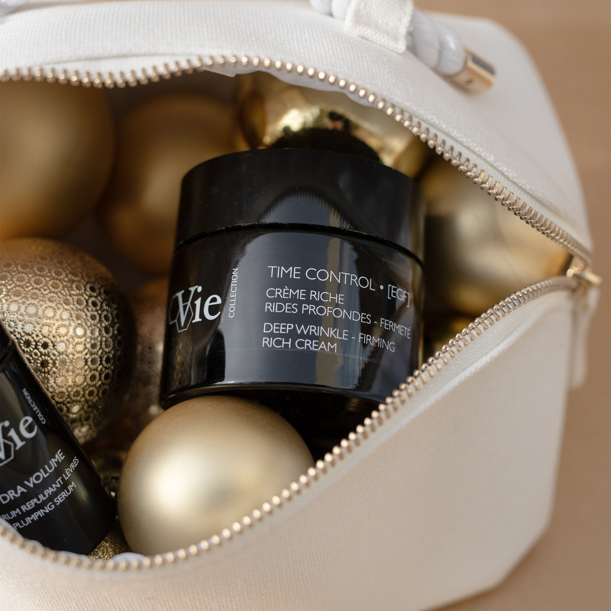 Close-up of Vie Collection Time Control Deep Wrinkle Firming Rich Cream in a white pouch surrounded by gold Christmas baubles.