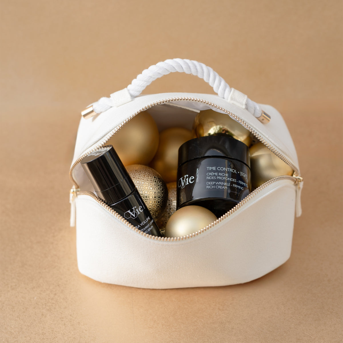 Vie Collection Time Control cream and Hydra Volume Lip Plumping Serum in an open white pouch with gold Christmas baubles.