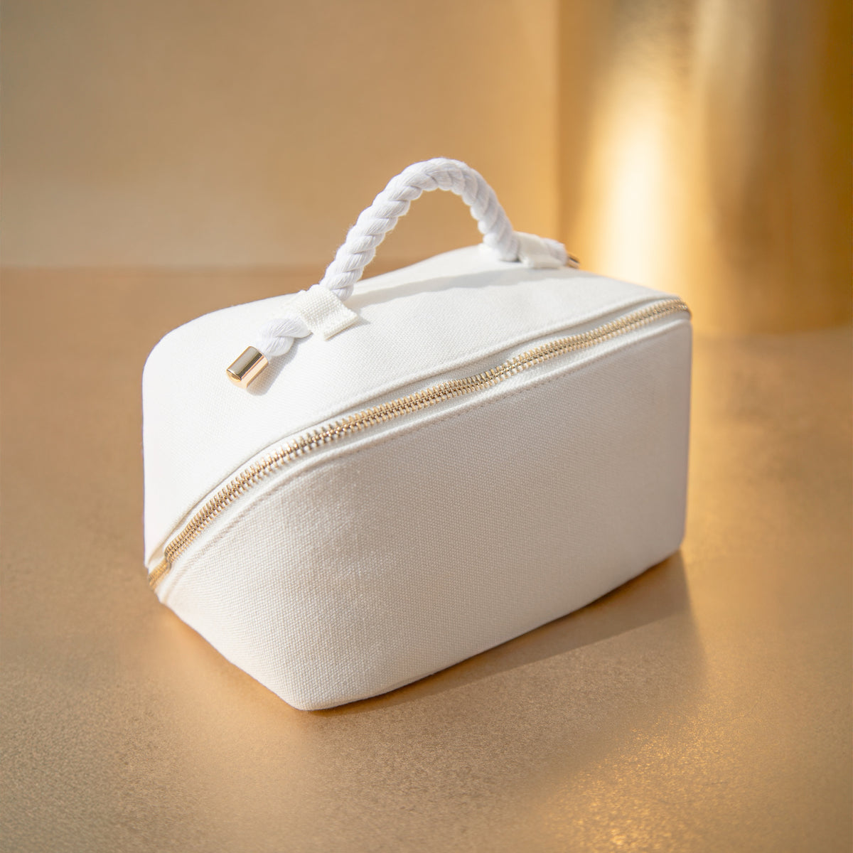 White Vie Collection gift pouch with a twisted rope handle and gold zip on a warm gold background.